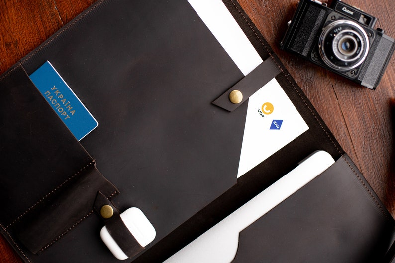 May include: A brown leather portfolio with a passport, a white phone charger, and a white sheet of paper with the logos "Ukr" and "KAA" printed on it.