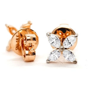 May include: A pair of rose gold stud earrings. Each earring features four marquise-cut, clear gemstones arranged in a flower shape. The earring backs are visible, with a post and butterfly clasp. The earrings are set against a white background.