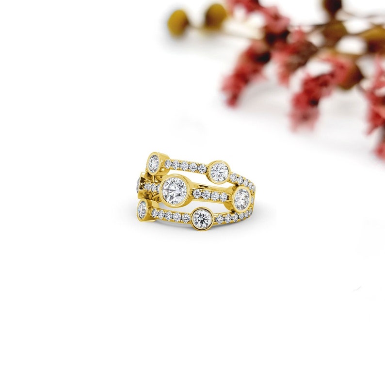 May include: A gold ring with a three-row design featuring round diamonds. The ring has a total of seven diamonds, with five larger diamonds and two smaller diamonds.
