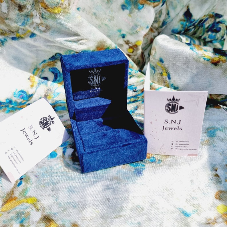 May include: A blue velvet ring box with a white label that says "S.N.J Jewels" and a crown logo. The box is open and empty.