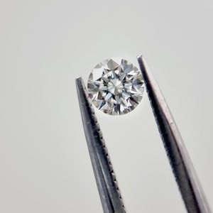 May include: A clear round diamond held by tweezers against a white background.