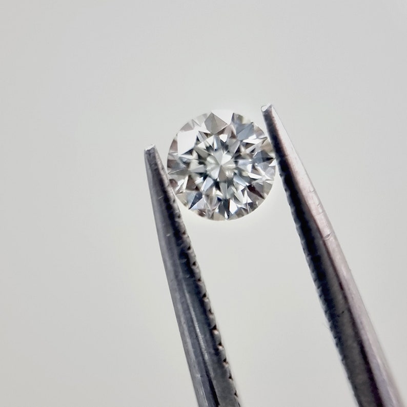 May include: A clear round diamond held by tweezers against a white background.