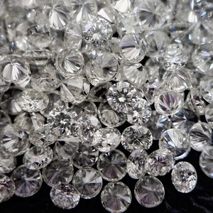 May include: A close-up image of a pile of round, clear, faceted diamonds. The diamonds are scattered on a black surface.