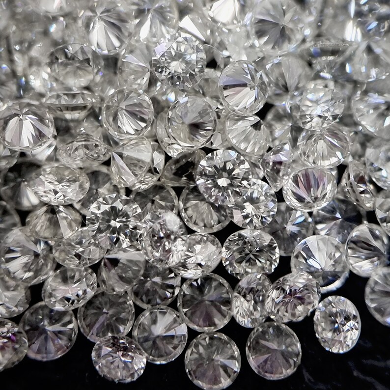 May include: A close-up image of a pile of round, clear, faceted diamonds. The diamonds are scattered on a black surface.
