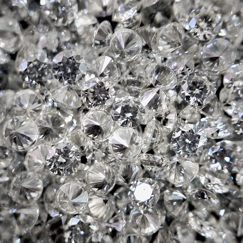 May include: A close-up image of a pile of loose, round, clear diamonds. The diamonds are faceted and sparkle brightly.