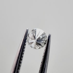 May include: A clear round diamond gemstone held in tweezers.