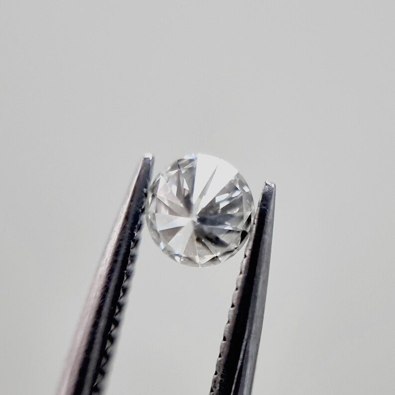 May include: A clear round diamond gemstone held in tweezers.