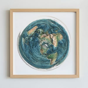 May include: A framed artwork featuring a detailed, textured depiction of Earth. The artwork showcases continents in shades of brown and green, surrounded by blue oceans. The piece is encased in a light-colored wooden frame, suitable for home decor.