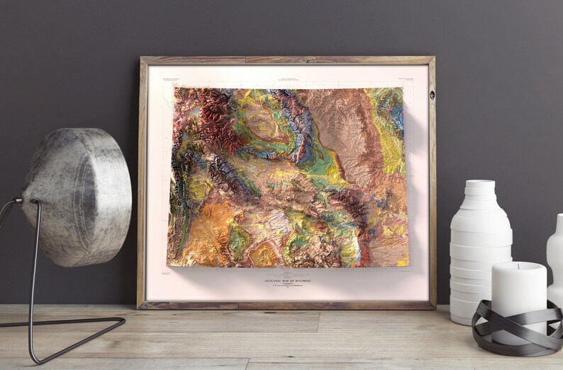 Puede incluir: Un mapa topogr&aacute;fico enmarcado de Wyoming con un dise&ntilde;o 3D texturizado y colorido. El mapa est&aacute; impreso en papel blanco y tiene un borde rosa claro. El marco es de madera y tiene un acabado marr&oacute;n claro.