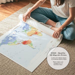 May include: A large, rolled-up world map print on matte paper featuring colorful continents against a light blue ocean background. The map displays various geographical regions in shades of green, yellow, and red, with clear text labels for countries and oceans visible across the surface.