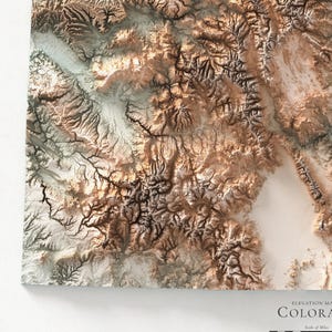 K&ouml;nnte beinhalten: Eine detaillierte, dreidimensionale H&ouml;henkarte von Colorado mit einem Reliefdesign in Braun-, Beige- und Wei&szlig;t&ouml;nen. Die Karte hebt das bergige Gel&auml;nde und die geografischen Merkmale des Staates hervor. Der Text "COLORADO" ist sichtbar.