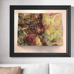 May include: Framed geological map of Colorado, featuring a detailed relief with a variety of colors including red, green, yellow, and brown. The map is set in a black frame and mounted on a light pink background. The title "GEOLOGIC MAP OF COLORADO" is visible.