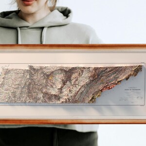 May include: A framed 3D relief map of the state of Tennessee. The map is in a brown wooden frame and shows the state's topography in detail.
