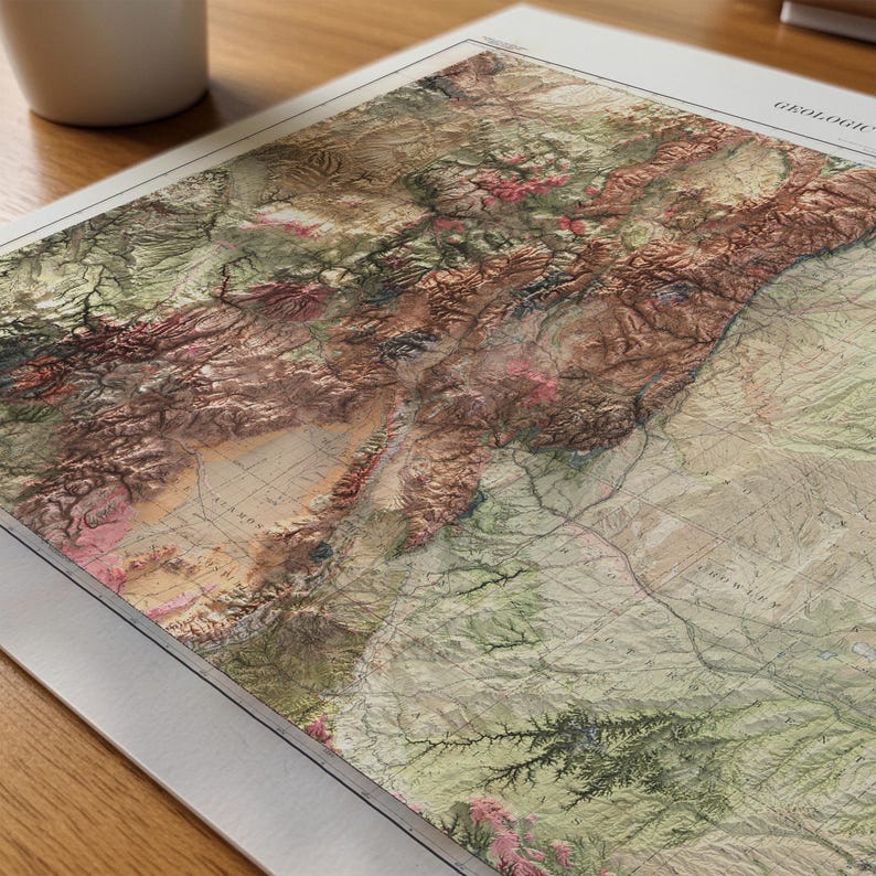 May include: A detailed, vintage-style geological map with a 3D relief effect. The map features a color palette of greens, browns, and pinks, depicting mountainous terrain and geographical features. The map is displayed on a white paper with a wooden surface.