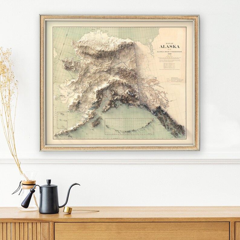 Framed custom Alaska map art displayed in a home office with a leather desk chair, vintage compass, and trail maps. The print focuses on the Inside Passage and Wrangell-St. Elias glaciers, inspiring wanderlust for outdoor enthusiasts or as a meaningful gift for someone planning their next Alaskan kayaking or fishing expedition.