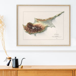 May include: A framed topographic map of Cyprus with a beige background and a brown, green, and beige colour scheme. The map shows the island's terrain with mountains and valleys.