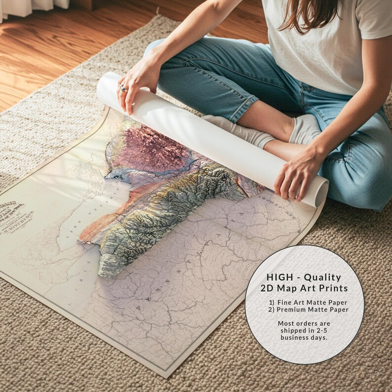 May include: A detailed map art print with a 3D topographic effect, featuring shades of beige, brown, and green. The map is partially rolled, revealing a section of the detailed artwork. The image includes text that says "HIGH - Quality 2D Map Art Prints".