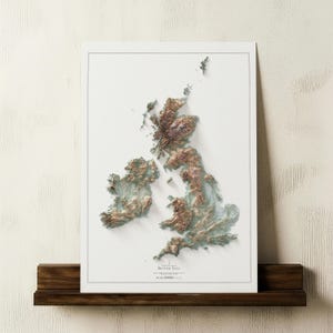 May include: A framed 3D relief map of the British Isles, showcasing the topography in shades of brown and green. The map is set against a white background and mounted on a dark wooden shelf. The title "British Isles" is visible.