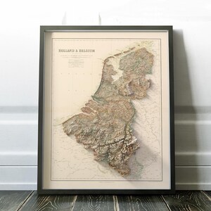 Pode incluir: Um mapa vintage da Holanda e da B&eacute;lgica, impresso em tons de marrom, verde e azul, com um efeito de relevo em relevo. O mapa est&aacute; emoldurado em uma moldura preta.