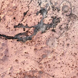 May include: An aerial view of a pink and grey landscape with a network of cracks and craters. The surface is textured and uneven, with a variety of sizes and shapes of craters.