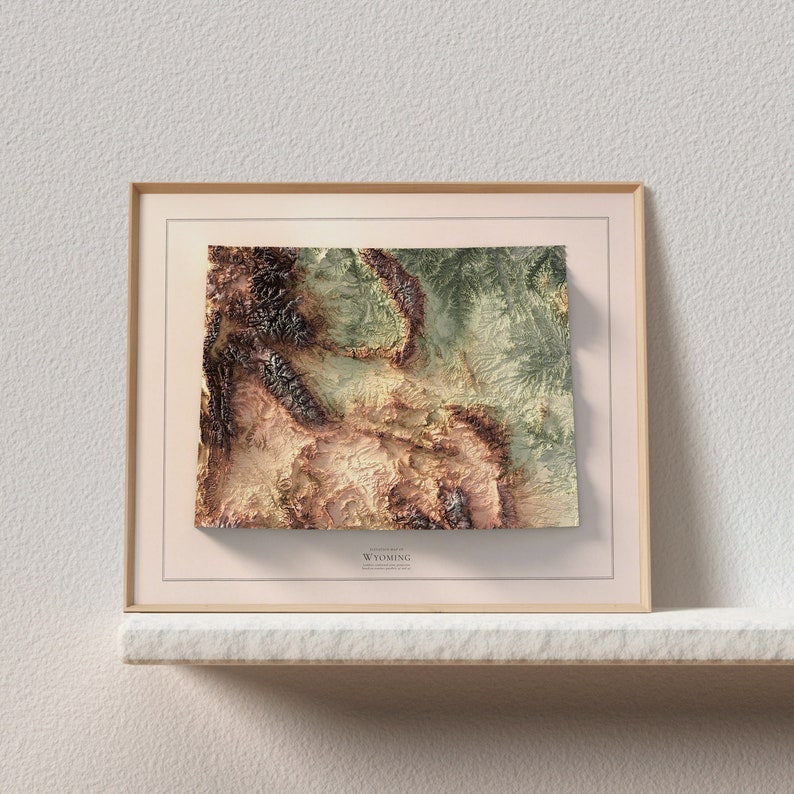 May include: A framed topographic map of Wyoming with a beige background and a gold frame. The map is in shades of brown, green, and beige, showing the state's terrain.
