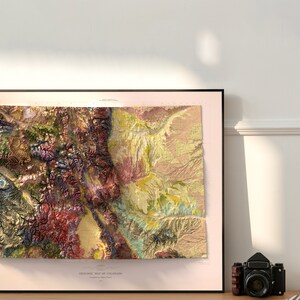 May include: A framed geologic map of Colorado, featuring a detailed relief with various colors representing different geological formations. The map is in a black frame, with the text "GEOLOGIC MAP OF COLORADO" at the bottom. A vintage camera sits nearby.
