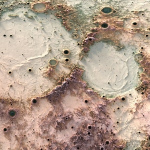 May include: A close-up of a cratered surface with a variety of colors, including beige, brown, and green. The surface is covered in small craters and has a rough texture.