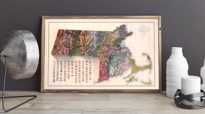 May include: A vintage map of the state of Massachusetts, showing the different geological formations in a colorful relief style. The map is framed in a wooden frame and has a white background.
