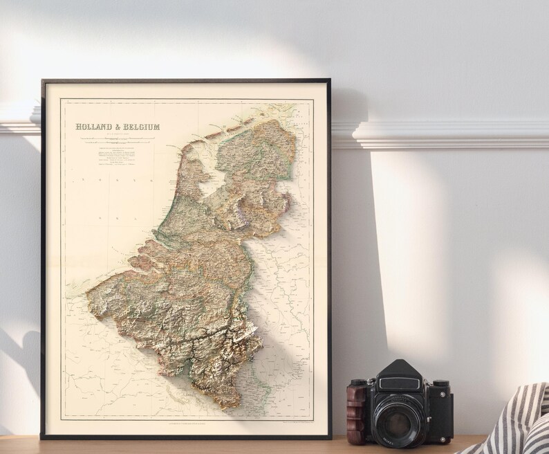 Pode incluir: Um mapa vintage da Holanda e da B&eacute;lgica, mostrando a topografia da regi&atilde;o. O mapa &eacute; impresso em tons de marrom, verde e bege, sobre um fundo branco. O t&iacute;tulo "Holland & Belgium" &eacute; impresso em preto no topo do mapa.