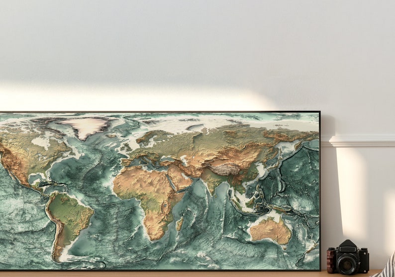 May include: A framed world map with a raised relief design, showing the continents and oceans in shades of green, brown, and blue. The map is framed in black and is hanging on a white wall.