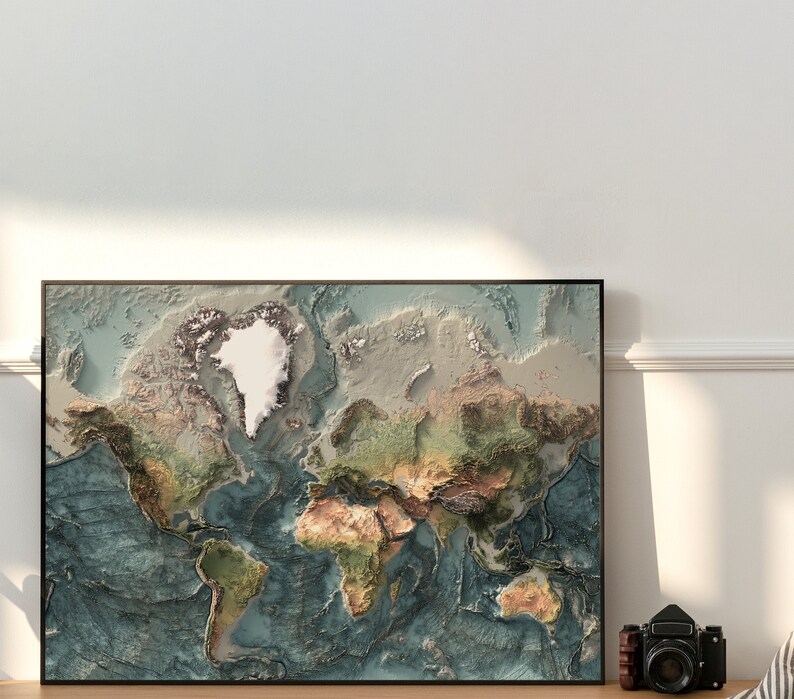 May include: A framed world map with a raised relief design, showing the continents and oceans in shades of blue, green, brown, and white. The map is framed in black and is hanging on a white wall.