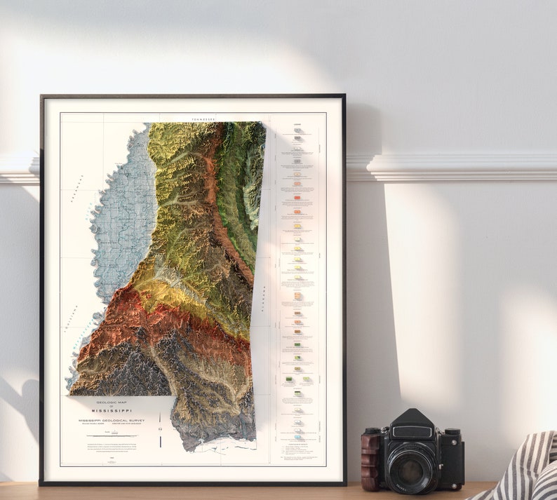 K&ouml;nnte beinhalten: Eine Reliefkarte von Mississippi im Vintage-Stil, die die Topographie des Bundesstaates in Gr&uuml;n-, Braun- und Blaut&ouml;nen zeigt. Die Karte ist schwarz gerahmt und hat einen wei&szlig;en Hintergrund mit einer Legende der geologischen Formationen.