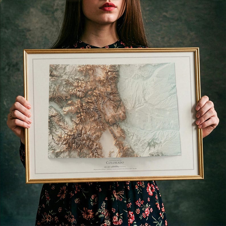 K&ouml;nnte beinhalten: Gerahmte topografische Karte von Colorado mit detaillierter Reliefschattierung in Braun-, Beige- und Wei&szlig;t&ouml;nen. Die Karte befindet sich in einem goldfarbenen Rahmen mit wei&szlig;em Passepartout. Das Wort "Colorado" ist unten auf der Karte aufgedruckt.