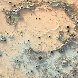 May include: A close-up of a textured surface with a light brown and blue color scheme. The surface is covered in small craters and crevices, resembling the surface of the moon.