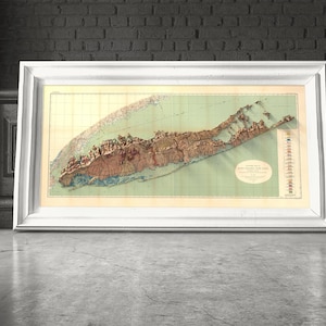 May include: A vintage map of Long Island, New York, printed in brown, green, and beige tones. The map is framed in a white frame and is displayed on a wall.