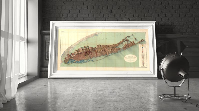 May include: A vintage map of Long Island, New York, printed in brown, green, and beige tones. The map is framed in a white frame and is displayed on a wall.