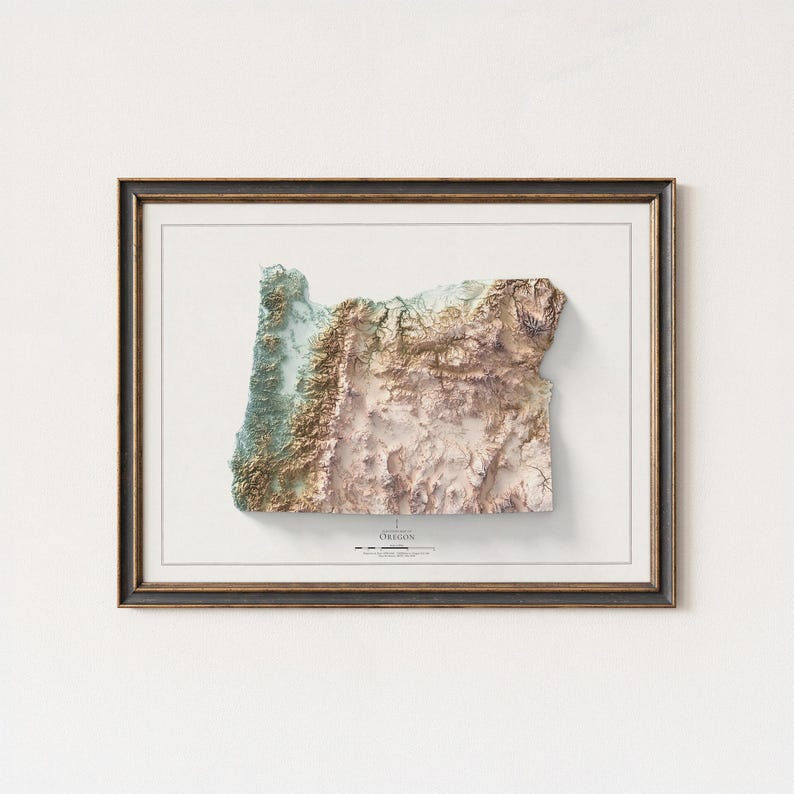 Puede incluir: Un mapa topogr&aacute;fico 3D enmarcado de Oreg&oacute;n, que muestra el terreno del estado con tonos de verde, marr&oacute;n y beige. El mapa est&aacute; sobre un fondo blanco y enmarcado en un marco oscuro y ornamentado. La palabra "OREGON" est&aacute; impresa en la parte inferior.