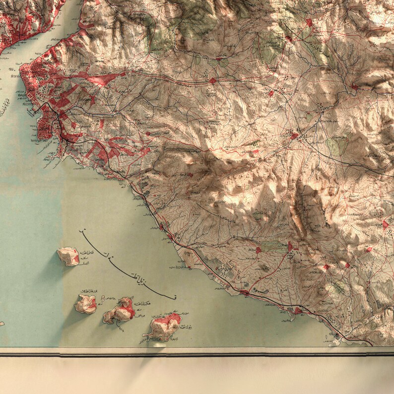 May include: An antique map of a mountainous region with red markings and Arabic text. The map shows a coastline with islands and a body of water. The map is printed on aged paper with a cream background.