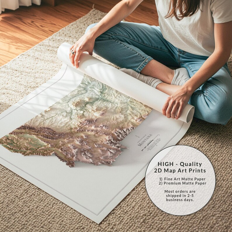 May include: A detailed 2D map art print of Montana, featuring topographical details in shades of brown, green, and beige. The print is on matte paper and is being unrolled. The text on the print reads "MONTANA".