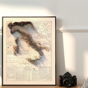 May include: A vintage-style map of Italy with a 3D embossed effect, showing the country's topography. The map is printed on a cream-colored paper with brown text and details. The map is framed in a black frame.