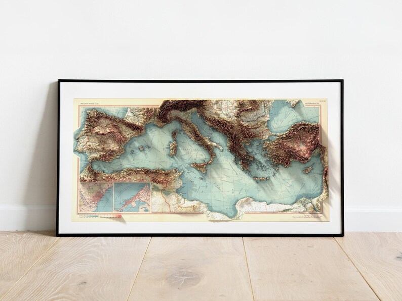 May include: A framed vintage map of the Mediterranean Sea with a 3D embossed effect. The map shows the coastline of Italy, Greece, Turkey, and other countries surrounding the sea. The map is printed on a cream-colored paper with brown and blue accents.