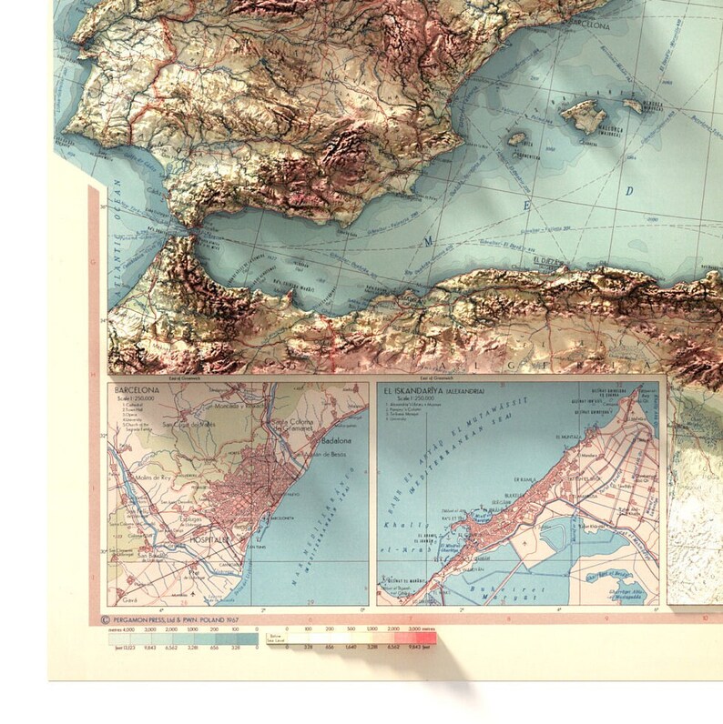 May include: A vintage map of Spain with a detailed inset map of Barcelona. The map is printed on a cream-colored paper with blue, green, and brown lines and text. The map shows the coastline, mountains, and cities of Spain.