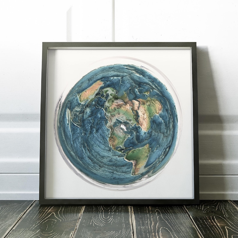 May include: Framed artwork featuring a detailed, textured depiction of Earth. The artwork showcases continents in shades of brown and green, surrounded by blue oceans. The piece is encased in a black frame, resting on a dark wooden surface.