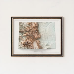 K&ouml;nnte beinhalten: Gerahmte 3D-Topografische Karte von Colorado mit detaillierter Reliefdarstellung in Braun-, Beige- und Wei&szlig;t&ouml;nen. Die Karte ist in einem dunkelbraunen Rahmen mit wei&szlig;em Passepartout eingefasst, und das Wort "Colorado" ist unten aufgedruckt.