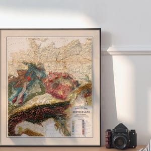 K&ouml;nnte beinhalten: Eine Reliefkarte Deutschlands im Vintage-Stil, die die Topographie des Landes mit verschiedenen Farben und Texturen zeigt. Die Karte ist schwarz gerahmt und tr&auml;gt den Titel "Geologische Karte Deutschlands".
