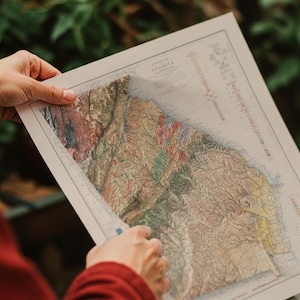 May include: A vintage map of Georgia, showing the state's topography with different colors and textures. The map is folded and being held by a person's hands.
