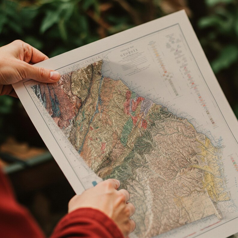 May include: A vintage map of Georgia, showing the state's topography with different colors and textures. The map is folded and being held by a person's hands.