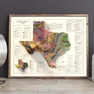 May include: A vintage-style map of Texas with a 3D relief effect, showing the state's geological formations in various colors. The map is framed in a wooden frame and is displayed on a wall.