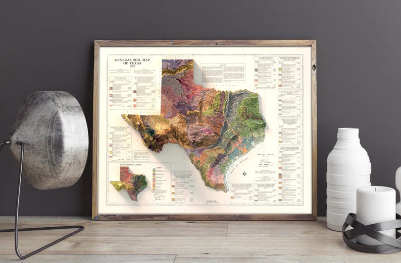 May include: A vintage-style map of Texas with a 3D relief effect, showing the state's geological formations in various colors. The map is framed in a wooden frame and is displayed on a wall.