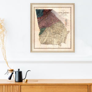 May include: An antique map of the State of Georgia, showing geological features. The map is printed on paper and framed in a light wood frame.